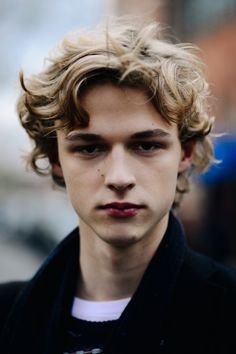 a close up of a person wearing a black jacket and white t - shirt with curly hair