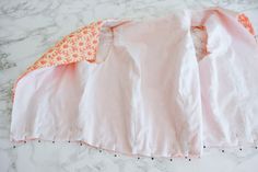 a pink shirt with an orange and white flowered design on the collar is laying on a marble surface