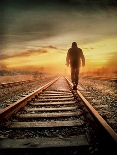 a man walking on train tracks towards the sun