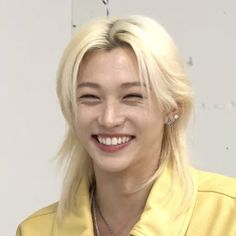 a woman with blonde hair smiling and wearing a yellow shirt in front of a white wall