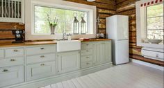 a kitchen with white cabinets and wooden walls, along with windows that look out onto the woods