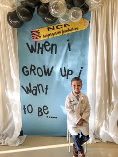 a young boy sitting on a chair in front of a bulletin board with balloon decorations