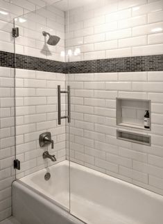 a white tiled bathroom with a glass shower door and bathtub in the corner,