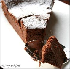 a piece of chocolate cake with powdered sugar on top and a spoon in the foreground