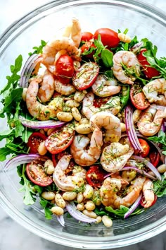 a glass bowl filled with shrimp, tomatoes and lettuce on top of a marble table