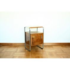 an end table with a glass top and metal legs on a wooden floor in front of a white wall