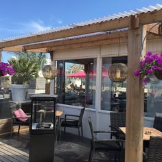 an outdoor restaurant with tables and chairs on the deck, covered in purple hanging flowers