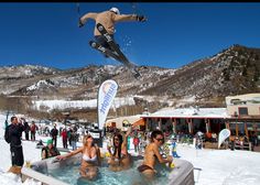 a man flying through the air while riding skis over a hot tub filled with people