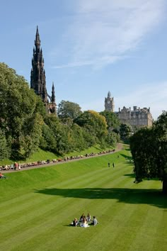 people are sitting on the grass in front of a castle