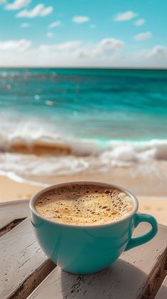 a cup of coffee sitting on top of a wooden table next to the ocean and beach