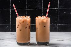 two glasses filled with iced coffee sitting on top of a marble counter next to each other