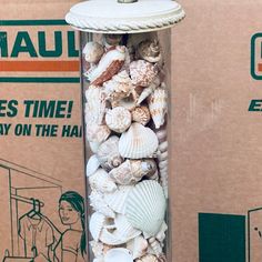 a glass vase filled with seashells on top of a table next to a cardboard box