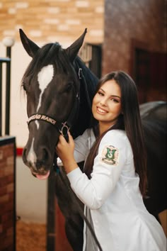 a woman standing next to a black and white horse in an indoor stable with her hand on the bridle