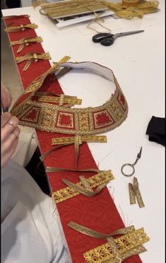 someone is working on an elaborate red and gold neck tie with scissors in the background