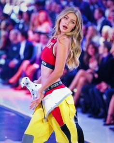 a model walks down the runway in a red top and yellow pants with white accents