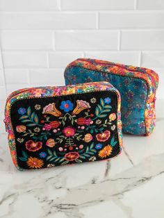 two colorful embroidered bags sitting on top of a white marble countertop next to each other