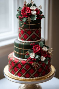 a three tiered cake decorated with red flowers and greenery on a gold plate