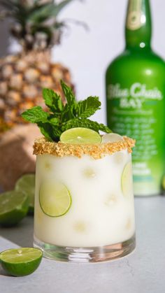 a drink with limes and mint garnish on the rim next to a pineapple