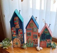 three small wooden houses sitting on top of a table next to a potted plant