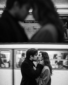 a man and woman kissing in front of a subway train at the station, black and white photograph