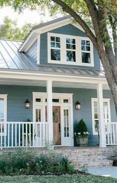 a blue house with white trim on the front door and porch, surrounded by trees