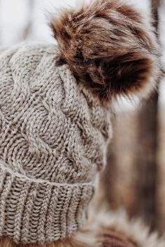 a close up of a person wearing a hat with fur pom - poms