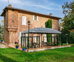 an old brick house with a gazebo in the front yard and green grass around it