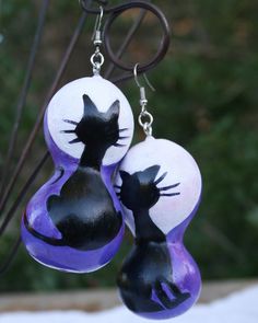 two black and white cat earrings hanging from a hook with purple glass beads on it