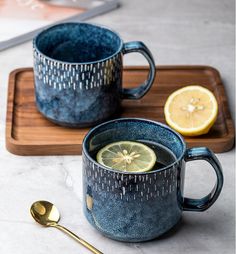 two blue mugs with lemon slices and spoon on a wooden tray next to each other