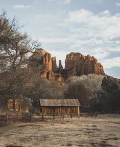 an old shack sits in the middle of a field with mountains in the back ground