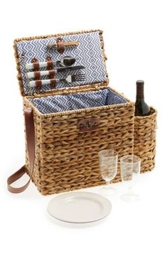 a wicker picnic basket with wine glasses and plates