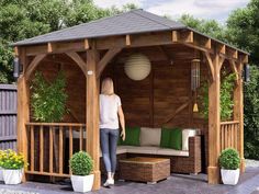 a woman standing under a wooden gazebo next to potted plants