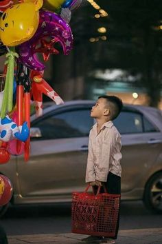 a young boy is standing in front of a bunch of balloons on the street and looking up