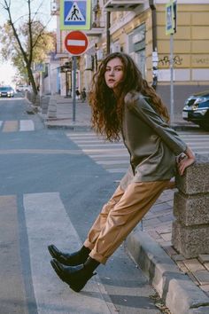 a woman leaning against a wall on the side of a street with her legs crossed