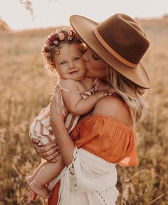 a woman holding a baby in her arms and wearing a hat on top of her head