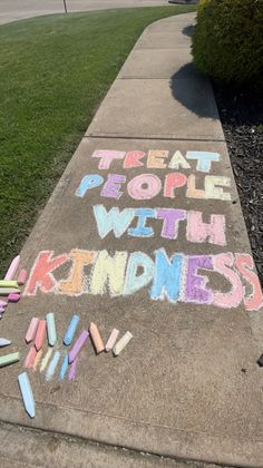 chalk writing on sidewalk that says treat people with kindness and crayons written in white