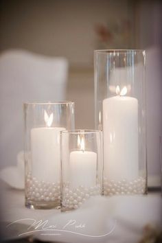 three white candles are sitting on a table with pearls in the glass vases next to them