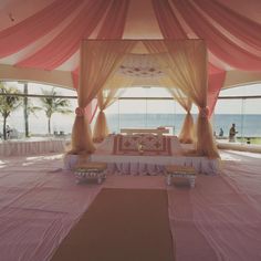 a bed sitting under a pink canopy next to the ocean