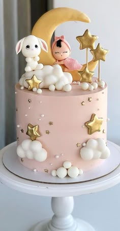 a pink cake decorated with stars, clouds and a baby rabbit on top is sitting on the moon