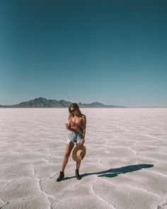 a woman standing in the middle of a desert with a hat and sunglasses on her head