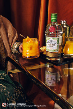 a glass table topped with a bottle of liquor and two glasses filled with orange juice