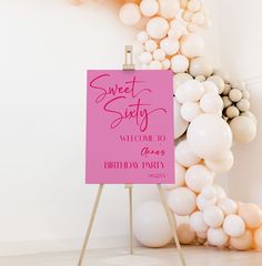 a pink sign sitting on top of a wooden easel in front of white balloons