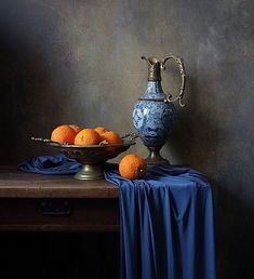 a blue and white vase sitting on top of a wooden table next to oranges