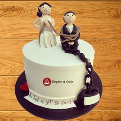 a wedding cake with two people holding hands and chains around it on top of a wooden table