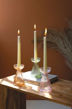 three lit candles sitting on top of a wooden table next to a book and potted plant