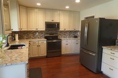 a kitchen with stainless steel appliances and white cabinets, wood floors, and granite counter tops