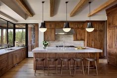 a large kitchen with wooden cabinets and counter tops, along with bar stools that match the hardwood flooring