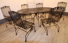 a glass table with four chairs around it on a hard wood floored area in front of a white wall