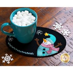 a mug filled with marshmallows sitting on top of a table next to snowflakes