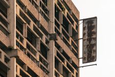 an old rusted sign hanging from the side of a tall building in front of a cloudy sky